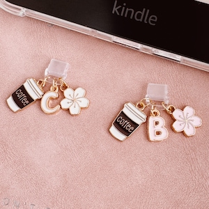 Op de afbeelding: Twee goudkleurige bedels met een koffiekopje, een letter en een bloem. Eén bedel heeft de letter "C" en de andere de letter "B". De koffiekopjes zijn wit met een zwarte band en het woord "coffee". De bloemen zijn wit met roze accenten.