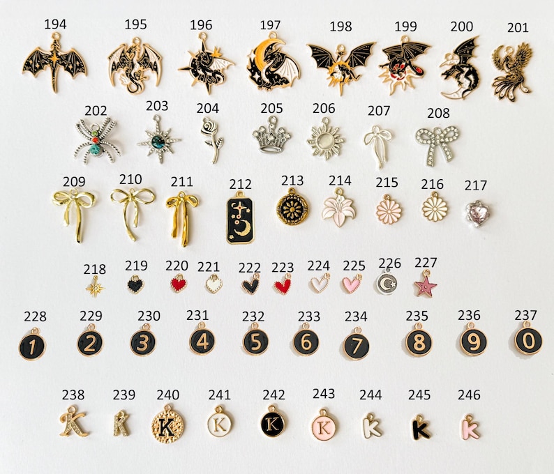 May include: A collection of small, decorative charms in various shapes and designs. Includes charms shaped like dragons, bows, flowers, hearts, and letters. The charms are in gold, black, white, and pink colors.