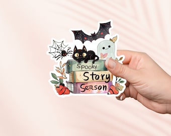 Könnte beinhalten: Eine schwarze Katze mit grünen Augen sitzt auf einem Stapel Bücher mit den Worten "Spooky Story Season" auf den Einbänden. Im Hintergrund sind ein weißer Geist und eine Fledermaus zu sehen. Außerdem gibt es Spinnweben und Blätter.