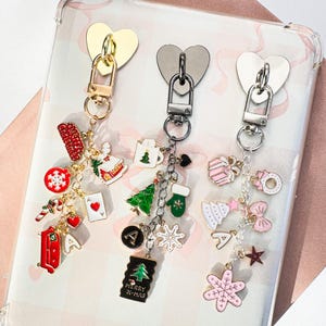 May include: Three Christmas-themed keychains with heart-shaped clasps. Each keychain features a variety of charms, including a snowflake, Christmas tree, and a red "Merry Christmas" banner. The keychains are gold, silver, and grey.