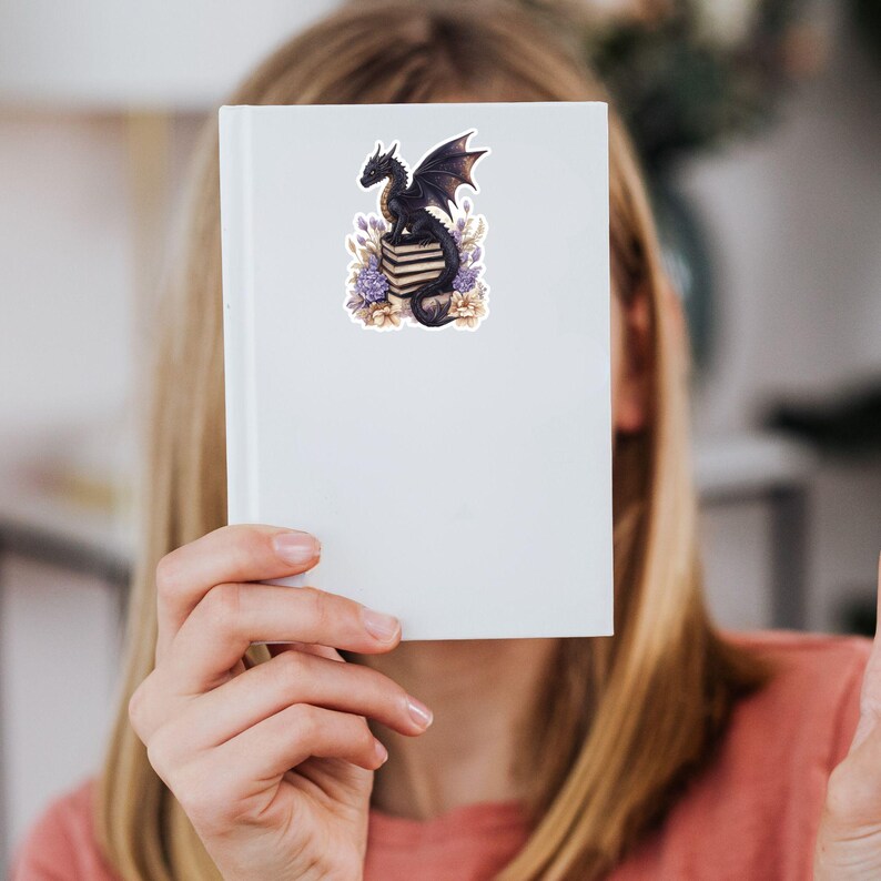 May include: A black dragon with purple wings sits on a stack of books with purple and white flowers around it.