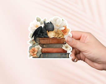 May include: A black and orange dragon couple sleeping on a stack of vintage books with white and orange flowers.