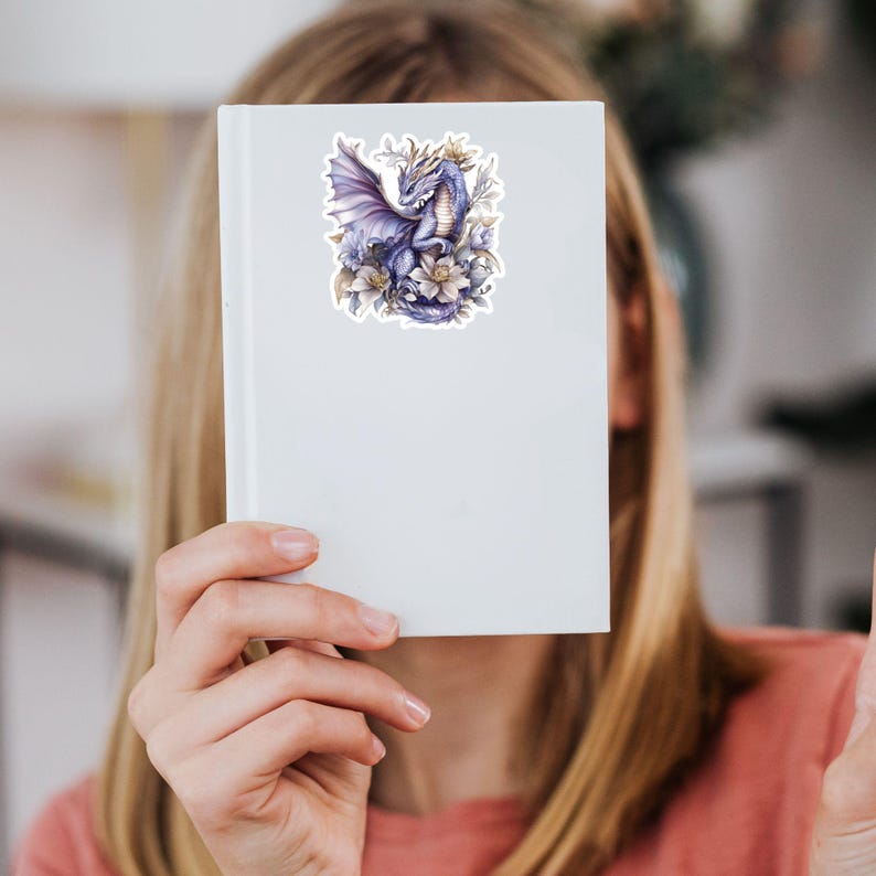 May include: A sticker featuring a purple dragon with gold accents, surrounded by white flowers. The dragon is depicted with its wings spread and its head turned to the side. The sticker is on a white background.
