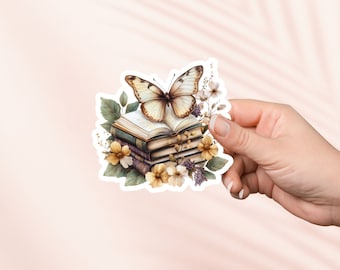 Puede incluir: Una pegatina que representa una pila de libros adornada con una mariposa y arreglos florales. La mariposa tiene alas marrones y crema. Los libros son en tonos verdes y morados, con flores amarillas y blancas.