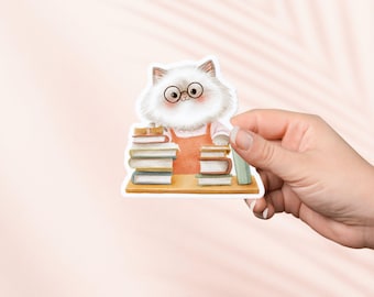 May include: A sticker featuring a white cat wearing glasses and an orange apron, surrounded by stacks of books. The cat is depicted in a cartoon style, with a friendly expression. The sticker is held by a hand against a soft pink background.