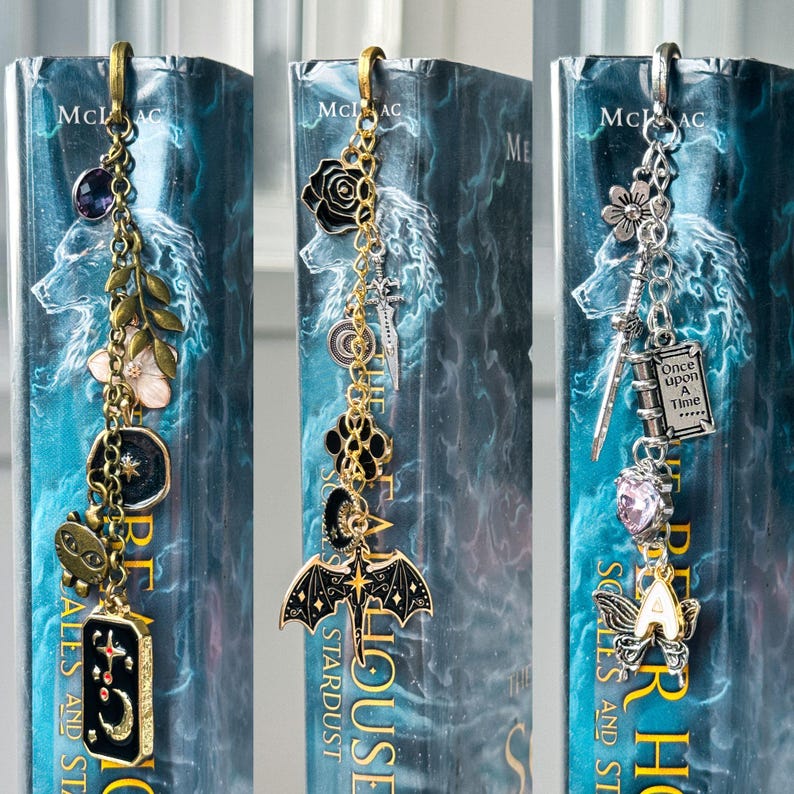 May include: Three decorative metal bookmarks with dangling charms. One has a purple gem, a flower, and a star. Another features a black rose, a bat, and a crescent moon. The third includes a flower, a sword, and a charm that says "Once Upon A Time".