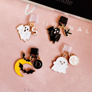 May include: Four Halloween-themed charms with gold-colored accents. The charms include a white ghost with the letter "S", a black ghost with the letter "K", a yellow crescent moon with bats and the letter "D", and a white ghost with the letter "R".