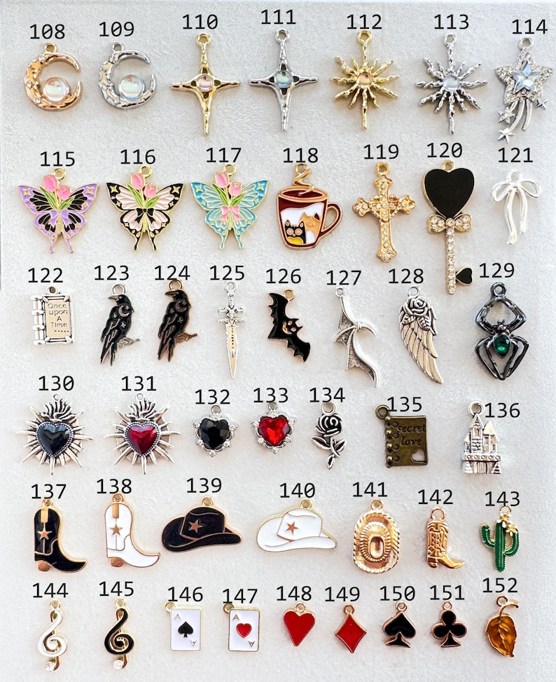 Op de afbeelding: Een verzameling zilver- en goudkleurige bedels met diverse ontwerpen, waaronder manen, kruisen, vlinders, een koffiekopje, een raaf, een vleermuis, een cowboylaars, een cactus en speelkaartsymbolen. Ideaal voor het maken van sieraden.