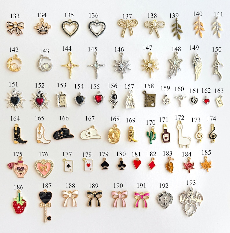 May include: A collection of small, decorative charms in various shapes and designs. The charms include bows, hearts, crosses, stars, and other symbols. They are made of metal and enamel, with a variety of colors and finishes.
