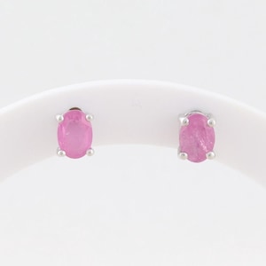 May include: A pair of silver stud earrings, each featuring a pink oval gemstone. The earrings are set against a white background, showcasing the vibrant color and shape of the stones. The studs are simple and elegant.