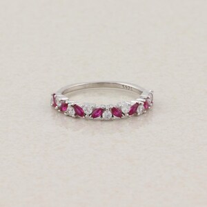 May include: A silver ring featuring an alternating pattern of marquise-cut pink stones and round clear stones set along the band. The interior of the band is clearly engraved with the text S925, indicating the metal composition of the jewellery piece.