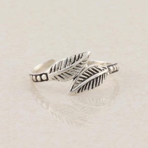 May include: A silver-toned open ring featuring two overlapping leaf-shaped elements with detailed veins. The band is accented with a series of small, raised circular beads on each side, creating a textured appearance across the metal surface.