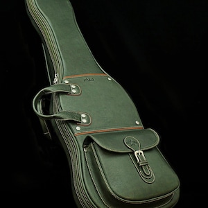 Könnte beinhalten: Eine dunkelgrüne Gitarrentasche aus Leder mit einer großen Fronttasche und einer silbernen Schnalle. Die Tasche hat einen braunen Lederbesatz und Nähte.