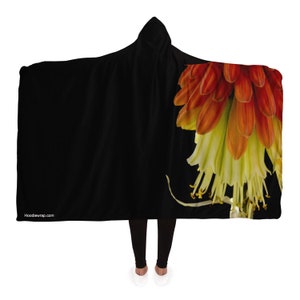 Peut inclure: Une couverture à capuche noire avec un motif de fleurs rouges et jaunes sur le côté droit. Le texte "HoodieWrap.com" est imprimé en blanc dans le coin inférieur gauche.