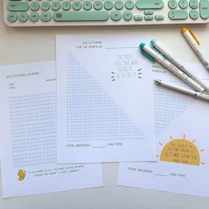 Könnte beinhalten: Eine Sammlung von Entrümpelungs-Tracker-Blättern mit motivierenden Zitaten und einer Tastatur. Die Blätter enthalten Punktmuster zur Fortschrittsverfolgung, mit Sätzen wie „Der effektivste Weg, es zu tun, ist, es zu tun“ und „Das Geheimnis, voranzukommen, ist, anzufangen“.