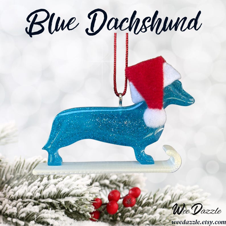 Handmade Dachshund Christmas Ornament made with high quality epoxy resin. The blue ornament comes with a red hanger and white sled with subtle silver glitter highlights on the front and dazzling glitter on the back.