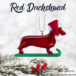 Handmade Dachshund Christmas Ornament made with high quality epoxy resin. The red ornament comes with a silver hanger and green sled with subtle red glitter highlights on the front and dazzling glitter on the back.