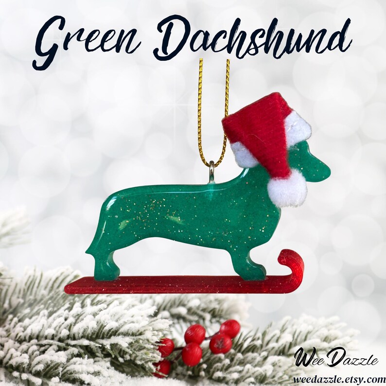 Handmade Dachshund Christmas Ornament made with high quality epoxy resin. The green ornament comes with a gold hanger and red sled with subtle gold glitter highlights on the front and dazzling glitter on the back.