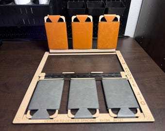 May include: A wooden jig for making slim koozies. The jig has three slots for holding the koozies in place while they are being sewn. The jig is labeled "Slim Koozie Jig" and has the text "Center to Center Spacing Y=194 X=121".
