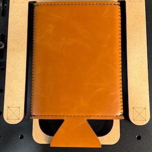 May include: A brown leather can cooler jig with the text "SLIM CAN COOLER JIG" printed on the top. The jig is made of wood and has a cutout for a can.
