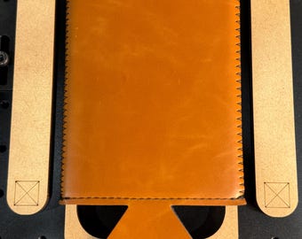 May include: A brown leather can cooler jig with the text "SLIM CAN COOLER JIG" printed on the top. The jig is made of wood and has a cutout for a can.