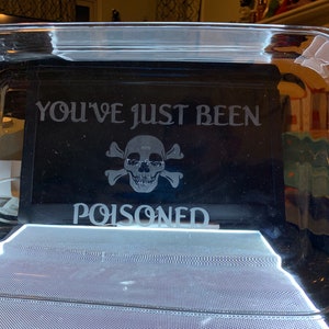 May include: A clear glass baking dish with a black background and the text "You've just been poisoned" etched into the glass. A skull and crossbones graphic is also etched into the glass.