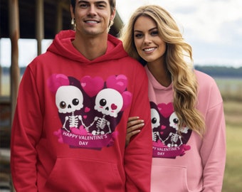 May include: A couple wearing matching red and pink hoodies with a graphic of two skeletons holding hands in front of a heart with the text "Happy Valentine's Day".