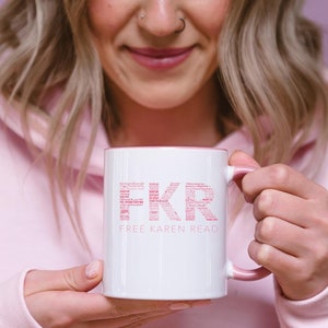 Puede incluir: Taza de cerámica blanca con borde y asa de color rosa. La taza tiene el texto "FKR FREE KAREN READ" impreso en letras rosas.