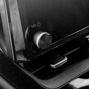 May include: Close-up of a car's dashboard, featuring a black volume control knob with a silver accent. The word "VOL" is visible. The image is in black and white.