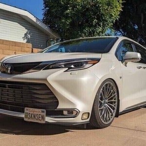 May include: A white minivan with black accents and a black grille. The car has a California license plate that reads "SKNSEN".