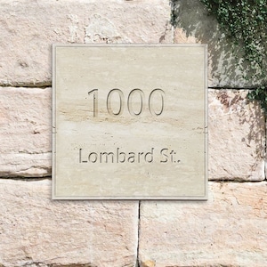 Op de afbeelding: Een stenen plaquette met het adres 1000 Lombard St. erin gegraveerd. De plaquette is bevestigd aan een bakstenen muur met groene wijnstokken die aan de rechterkant groeien.