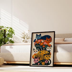 May include: A framed art print featuring a stack of stylized cats in various colors and patterns. The cats have floral and striped designs, with a black frame. The artwork is displayed in a bedroom setting.