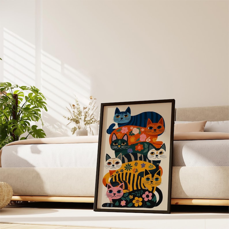 May include: A framed art print featuring a stack of stylized cats in various colors and patterns. The cats have floral and striped designs, with a black frame. The artwork is displayed in a bedroom setting.
