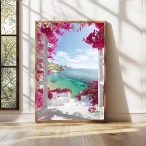 Puede incluir: Una impresión enmarcada de una vista costera escénica. La imagen muestra una ventana con flores de buganvillas de color rosa brillante que enmarcan un mar turquesa, edificios blancos y un cielo azul. La impresión está en un marco de madera y está apoyada contra una pared.