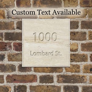 Könnte beinhalten: Eine quadratische beige Steinplatte mit der eingravierten Nummer 1000 und dem Text Lombard St. Die Platte enthält oben den Text Custom Text Available. Die Oberfläche des Steins hat ein natürliches, strukturiertes Aussehen mit sichtbaren Variationen.