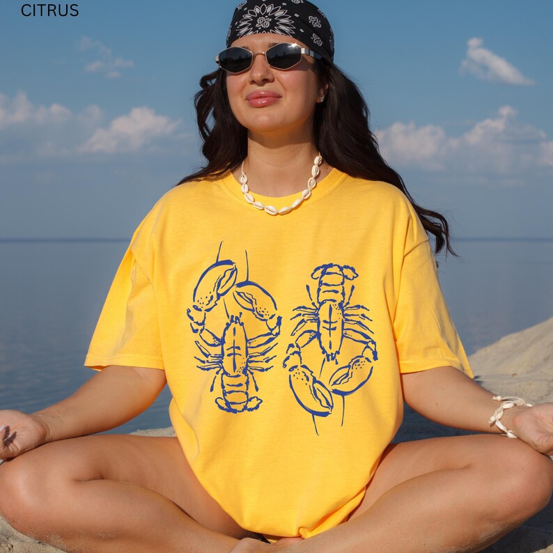 May include: Yellow t-shirt with a blue lobster graphic. The word "CITRUS" is in the top left corner. The shirt is a bright yellow color and has a relaxed fit. The lobster design is a detailed illustration.