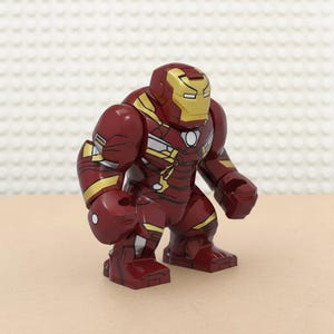 Pu&ograve; includere: Una action figure di Iron Man rossa e oro. La figura ha un elmetto dorato con un design a occhi rettangolari e un corpo rosso con dettagli dorati. La figura &egrave; in piedi.