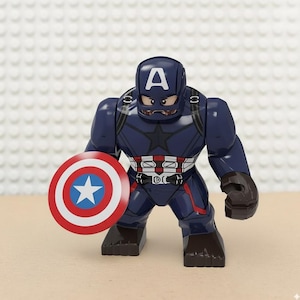 May include: A Captain America action figure in a dark blue suit with a white "A" on the helmet. The figure holds a red, white, and blue shield with a white star. The figure has a black star on the chest.