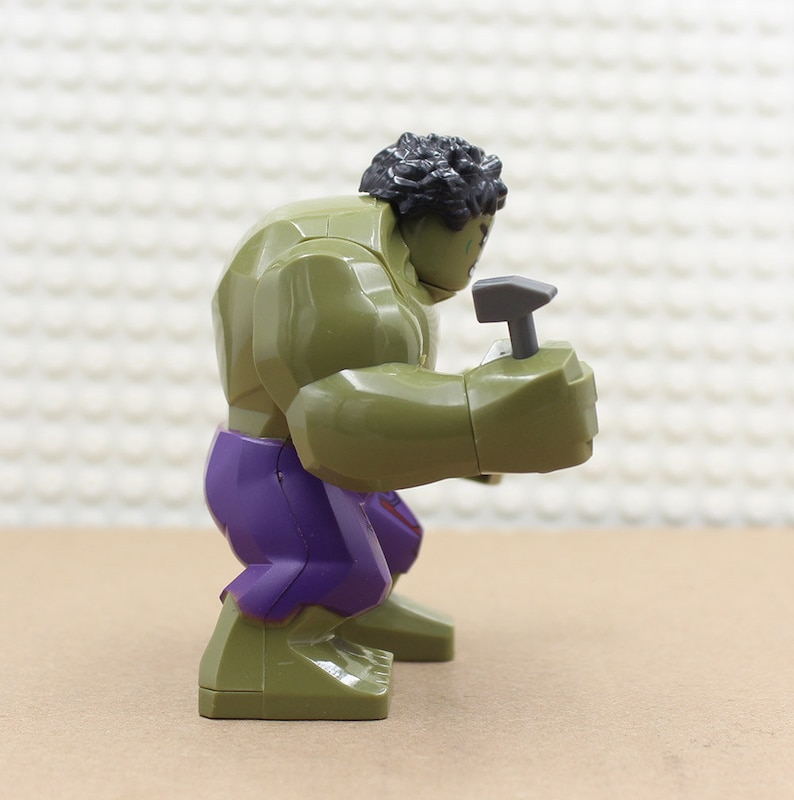 Puede incluir: Una minifigura Lego Hulk verde y morada sosteniendo un martillo gris.