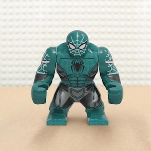 May include: A teal and gray action figure of a superhero with a spider-web design on the head and chest. The figure has a muscular build, with a black spider emblem on the chest and gray accents on the legs and arms.