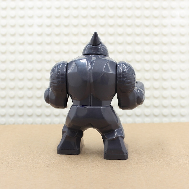 Puede incluir: Una figura de juguete de pl&aacute;stico gris de un rinoceronte, con un cuerno en la cabeza y una construcci&oacute;n muscular. La figura est&aacute; en posici&oacute;n de pie con los brazos a los lados.