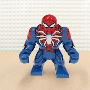 May include: A blue and red Spider-Man action figure. The figure has a red mask with white eyes and a white spider emblem on the chest. The figure is in a standing pose and is made of plastic.