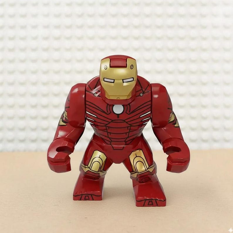 May include: A red and gold Iron Man action figure. The figure has a red body with gold accents on the helmet, shoulders, and legs. The figure is standing upright with its arms at its sides.