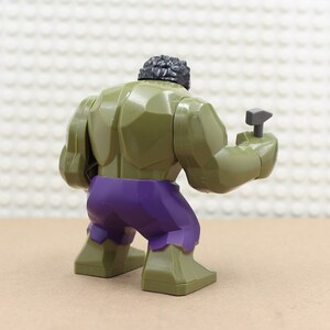 Puede incluir: Minifigura Lego verde y morada del Hulk, sosteniendo un martillo gris en su mano derecha.