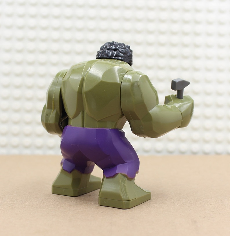 Puede incluir: Minifigura Lego verde y morada del Hulk, sosteniendo un martillo gris en su mano derecha.