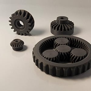 May include: A set of four gray plastic gears. The largest gear has a ring of smaller gears inside it. The gears are all interlocked.