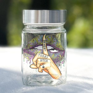 May include: A clear glass jar with a silver lid featuring a colorful graphic of a purple and pink lip with a finger over it. The finger has the words "NOT TODAY BITCH" written on it and a marijuana leaf tattoo. The background is a glittery pattern of green, yellow, and purple.