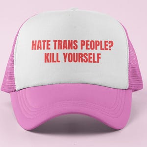 May include: A pink and white trucker hat featuring a mesh back and a solid front panel. The front panel displays the red text HATE TRANS PEOPLE? KILL YOURSELF in a bold, sans-serif font. The hat has a curved pink brim and a structured crown.