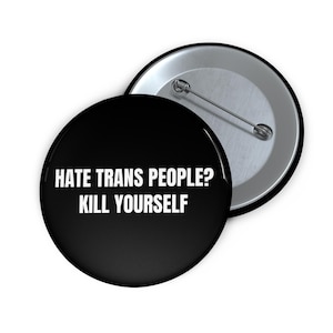 May include: A round pin-back button with a black background and white text that reads HATE TRANS PEOPLE? KILL YOURSELF. The button has a metallic silver back with a pin mechanism visible on the second button positioned behind the first one.