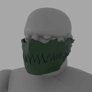 Puede incluir: Una máscara verde oscuro con un diseño dentado en forma de dientes que cubre la zona de la boca. La máscara se lleva en una cabeza de maniquí gris, con la parte superior de la cabeza y los hombros visibles. Los bordes de la máscara tienen un aspecto texturizado y orgánico.